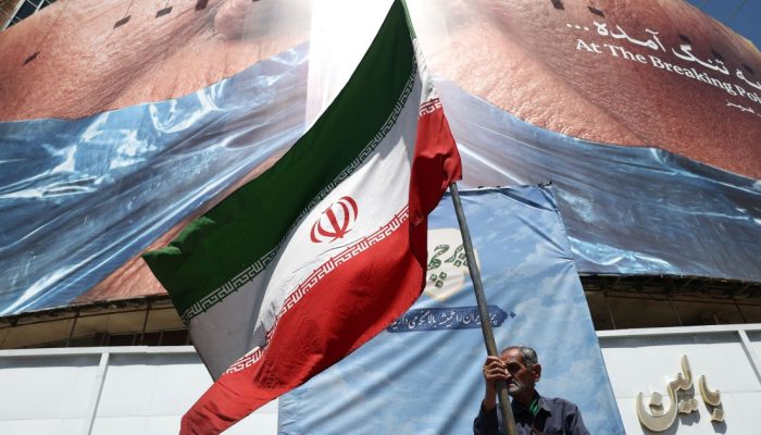 Homem-segura-bandeira-iraniana-perto-de-outdoor-anti-EUA-representando-o-presidente-dos-EUA-Donald-T.jpeg